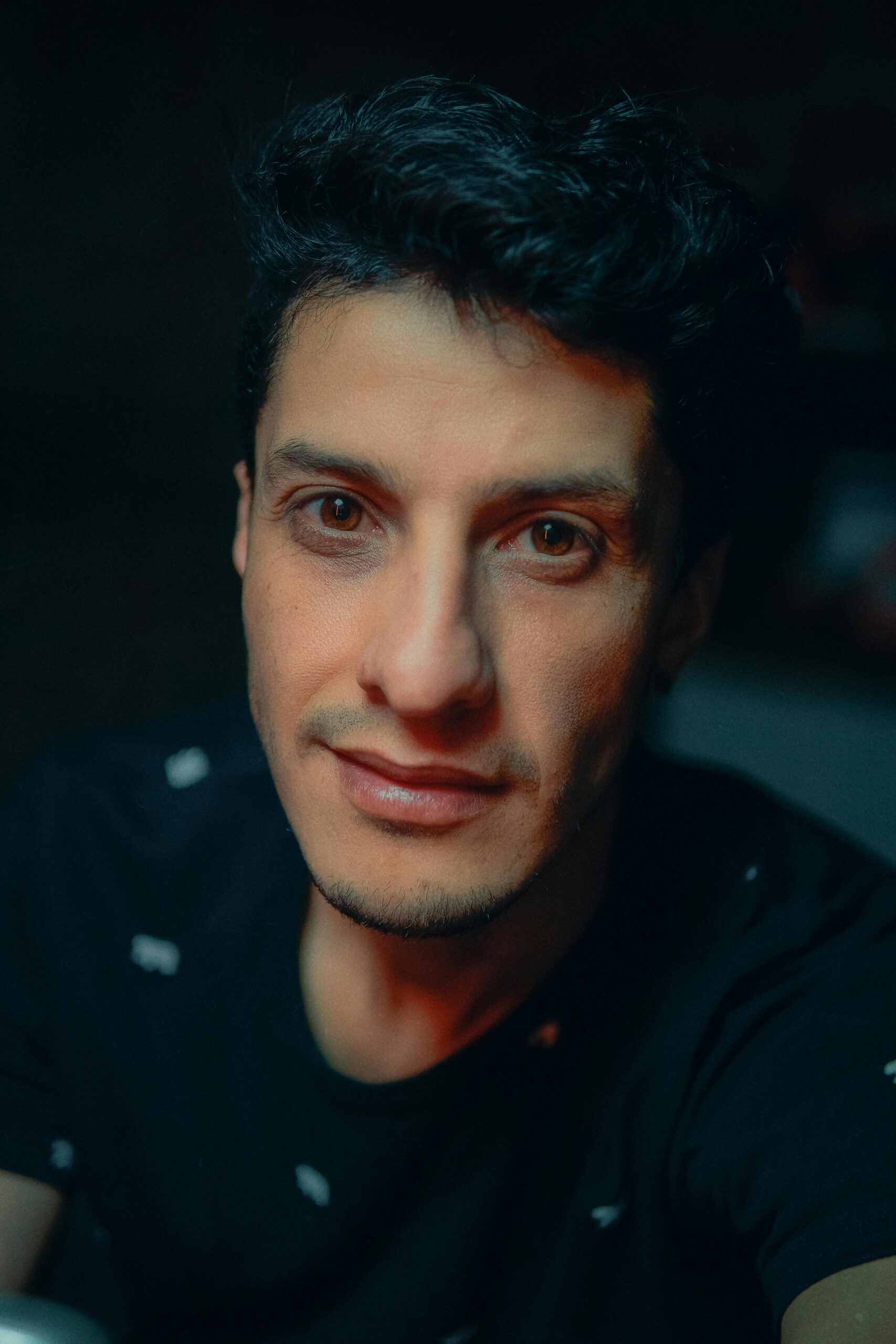 Close-up portrait of a smiling man wearing a black shirt, showcasing natural expressions and warm lighting.